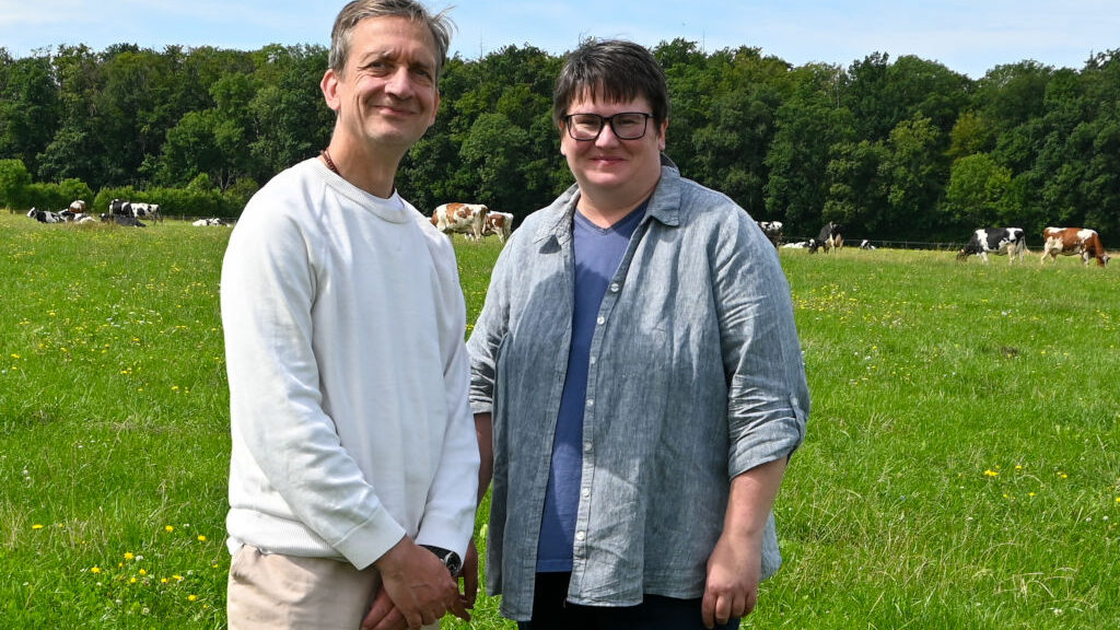 Sebastian Lück und Anne Wetzel (Vorstand Bürgermolkerei Weimar) stehen auf einer Weide, im Hintergrund Bio-Kühe.